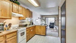 Cocina con armarios de madera, estufa y lavamanos. Zona de comedor con sofá y alfombra.