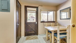 Una habitación pequeña con una puerta de madera, una ventana que da a un edificio y una mesa con sillas.