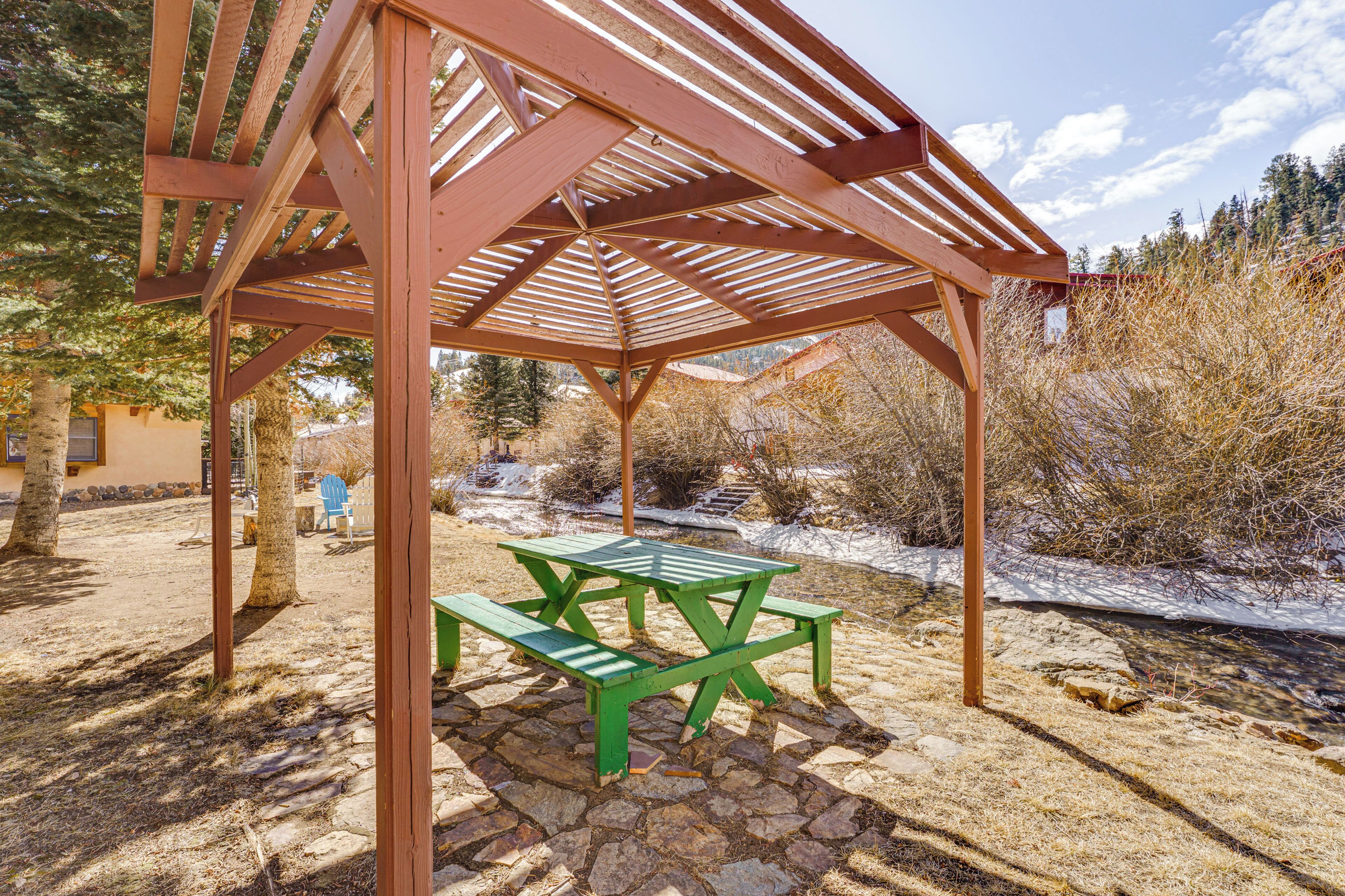 Una pérgola de madera con una mesa de picnic en un entorno natural.