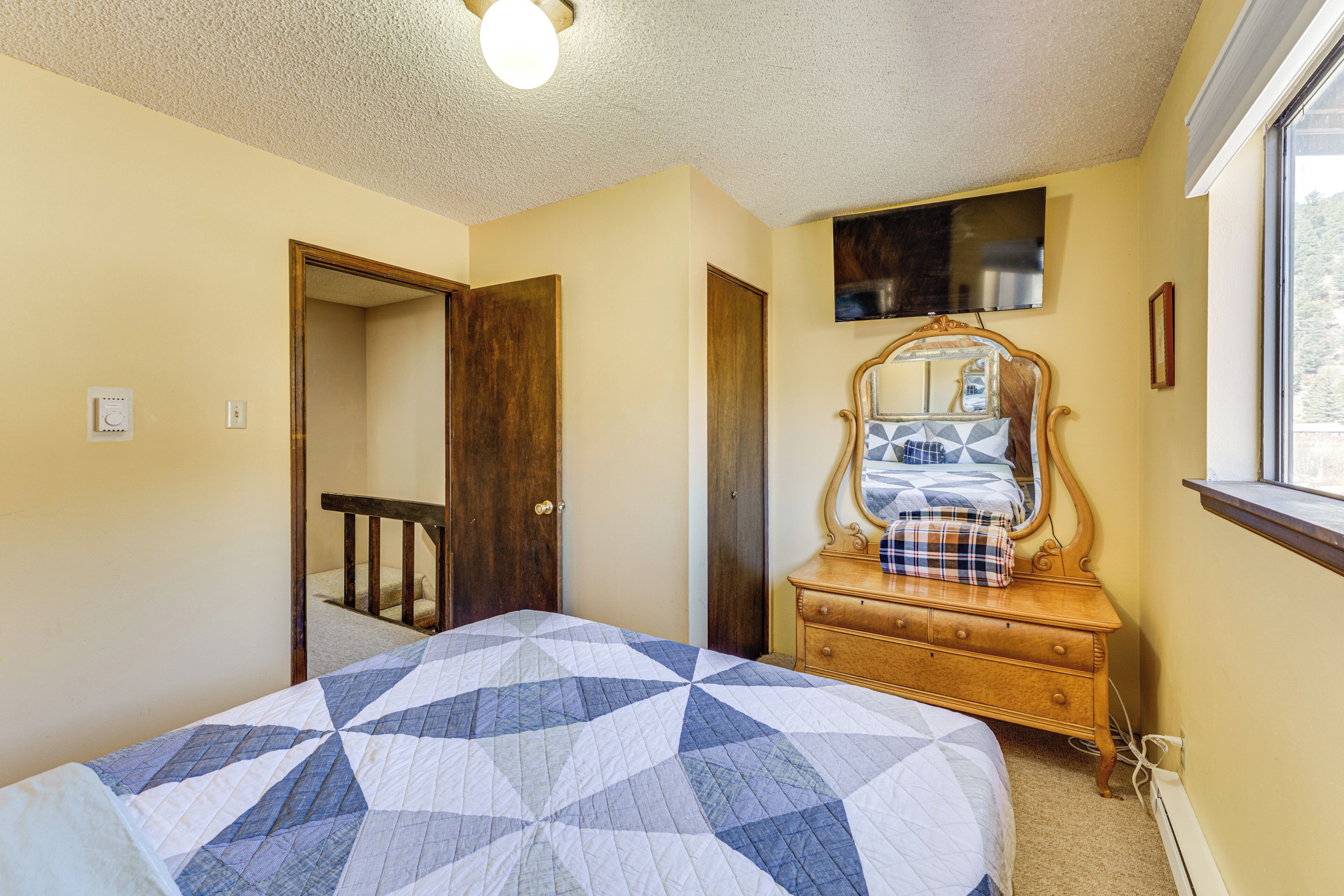 Un dormitorio con cama, cómoda, espejo y una puerta que da a otra habitación.
