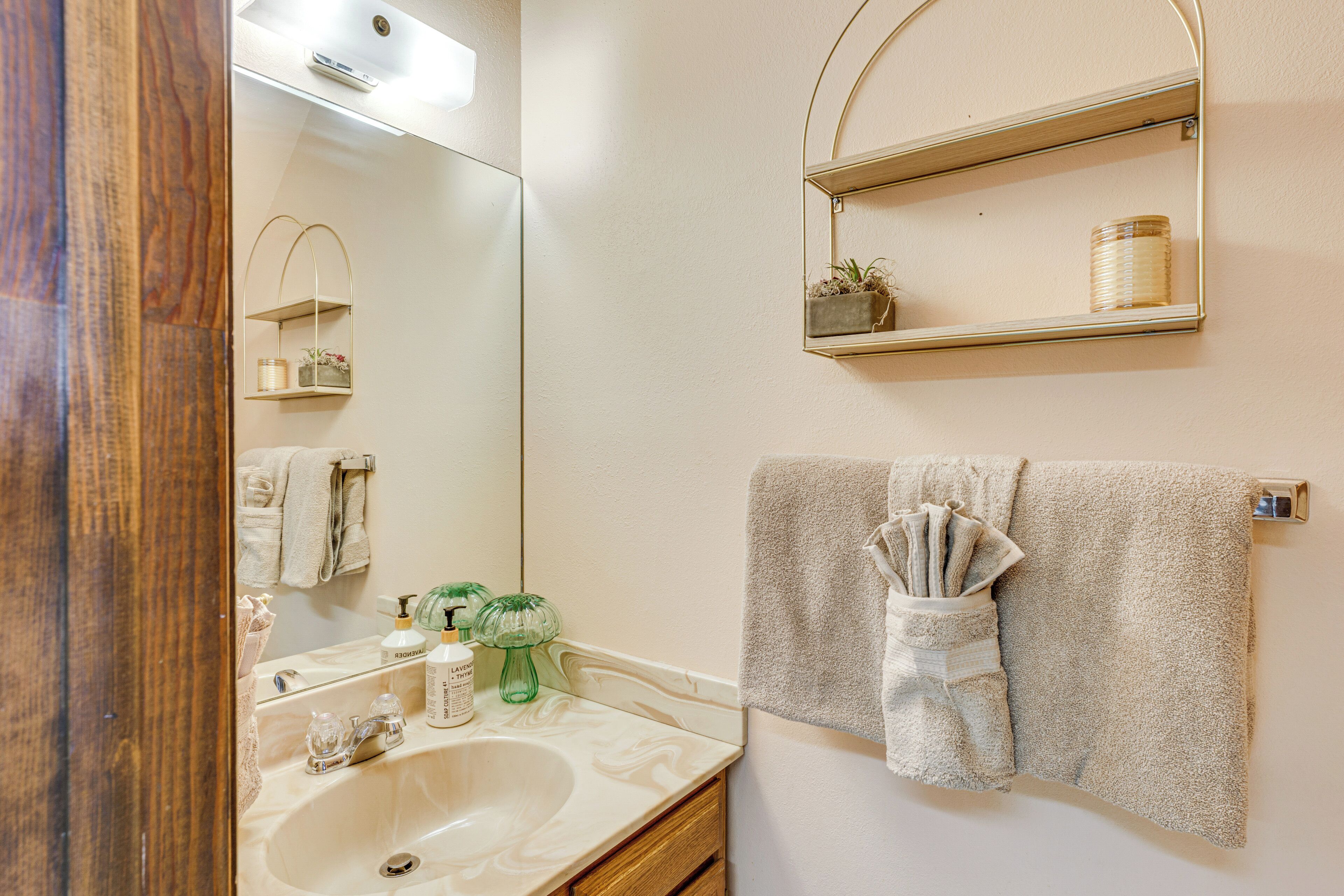 Une salle de bain équipée d’un lavabo, d’un miroir, d’un porte-serviettes et d’une étagère sur laquelle est posée une plante.