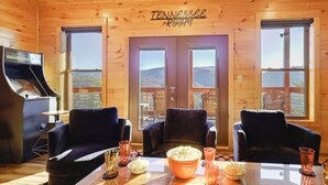A cozy room with wooden walls, two large windows, a piano, and a table with chairs and bowls of popcorn. - Majestic Mountain Views: Sevierville Escape! (Sevierville)