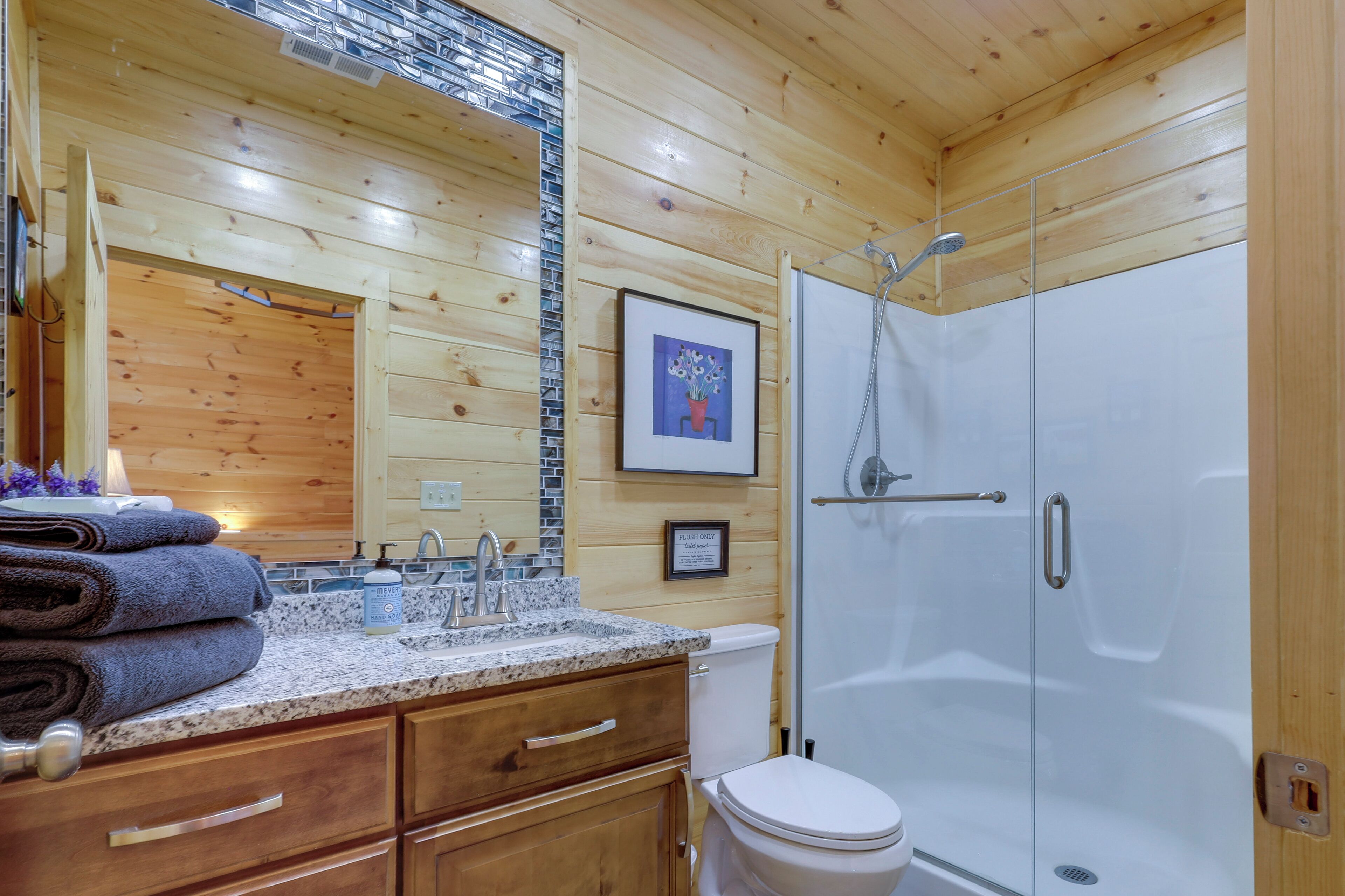 A wooden-paneled bathroom with a sink, mirror, toilet, and shower.