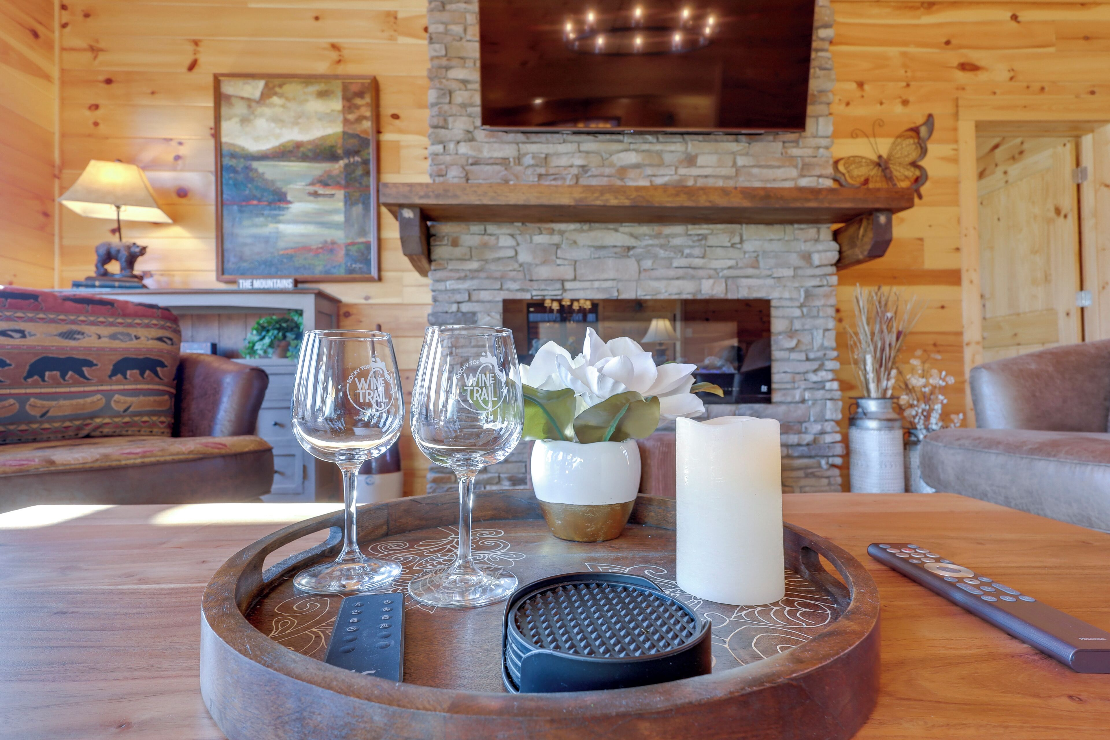 A wooden interior with a stone fireplace, a tray with glasses, a candle, and a remote control.