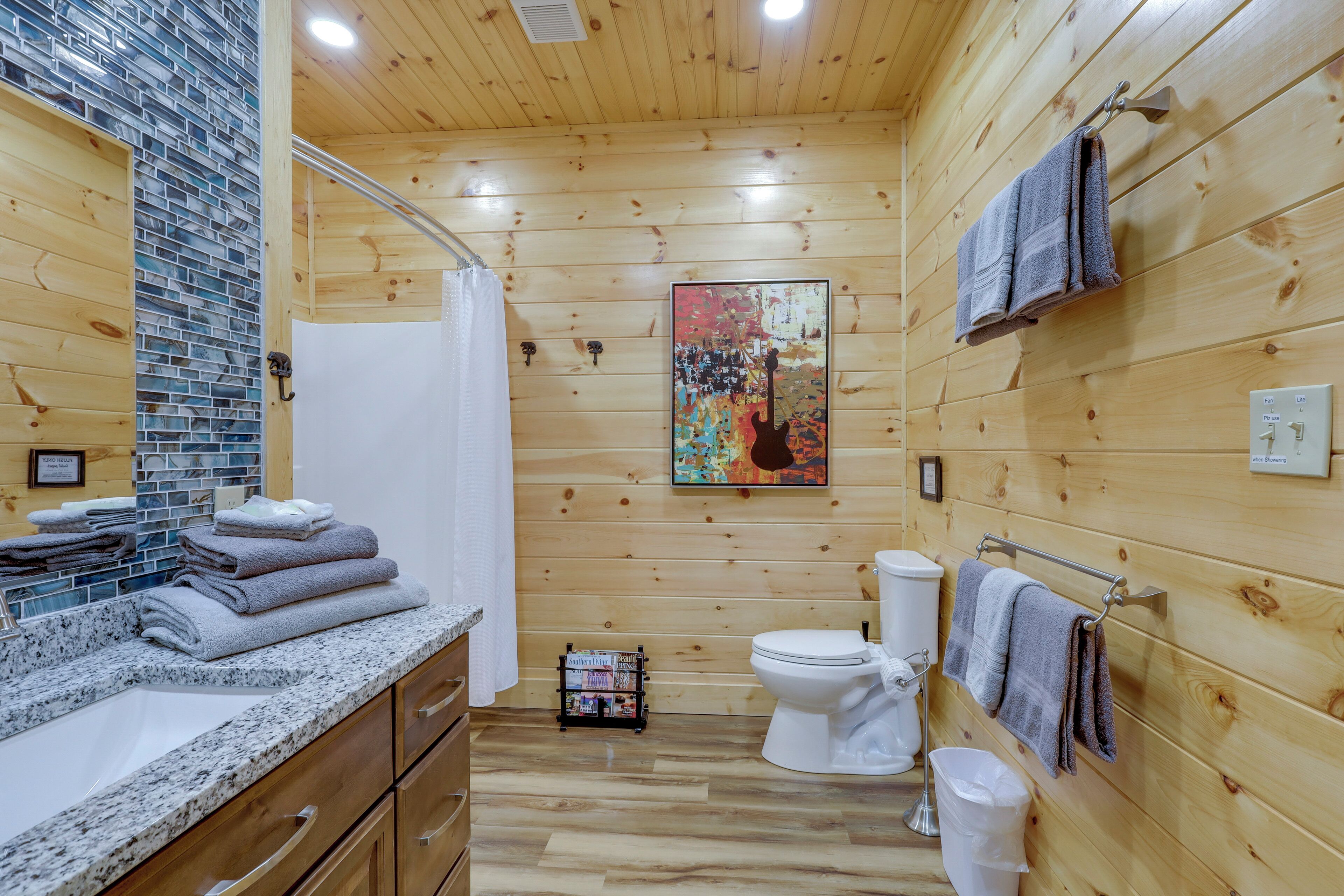Un baño con paneles de madera, que incluye un lavamanos, inodoro y ducha. Hay toallas apiladas en el mostrador y un perchero con toallas colgando en la pared.
