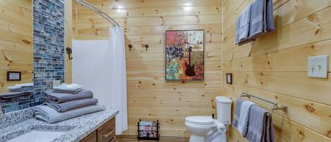 Un baño con paneles de madera, que incluye un lavamanos, inodoro y ducha. Hay toallas apiladas en el mostrador y un perchero con toallas colgando en la pared.
