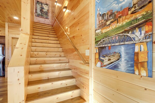 Un escalier en bois, avec une peinture représentant un pont et un navire accrochée au mur.