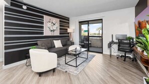 A modern living room with a sofa, armchair, and coffee table, a desk with a computer, and a large window with a view. - Chill 2BR Near ASU, Pool, Grill, Pkng, Pet Frndly (Tempe)