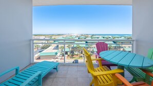 Ein Balkon mit bunten Adirondack-Stühlen und einem Tisch, mit Blick auf ein Resort mit Gebäuden und einem Strand.