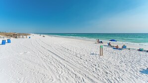 Ein Strand mit weißem Sand, klarem blauen Wasser und einer Holzstege.