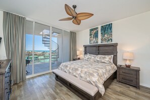 Relax in this serene bedroom with a large bed, nightstand, and bench, offering a peaceful retreat with a balcony and outdoor access.