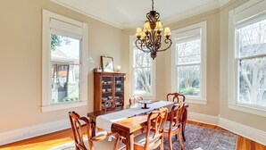 A dining room with a wooden table, chairs, a chandelier, and a window with a view of trees. - Walk to Mississippi River & Dtwn: Historic Haven! (Natchez)