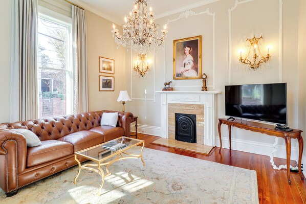 Una sala de estar con un sofá de cuero, una mesa de centro de vidrio, una chimenea, un televisor y apliques de pared.