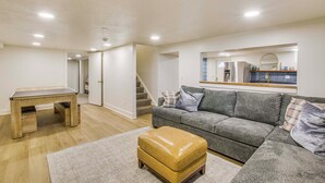 Ein modernes Wohnzimmer mit einem grauen Sofa, einem Holztisch und einem Ledersitzhocker.