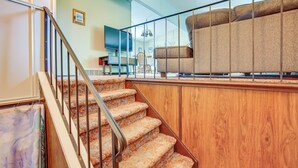A staircase with a wooden handrail leading to a living area with a sofa and a television. - 8 Mi to Crystal Mountain: Peaceful Up North Home (Copemish)