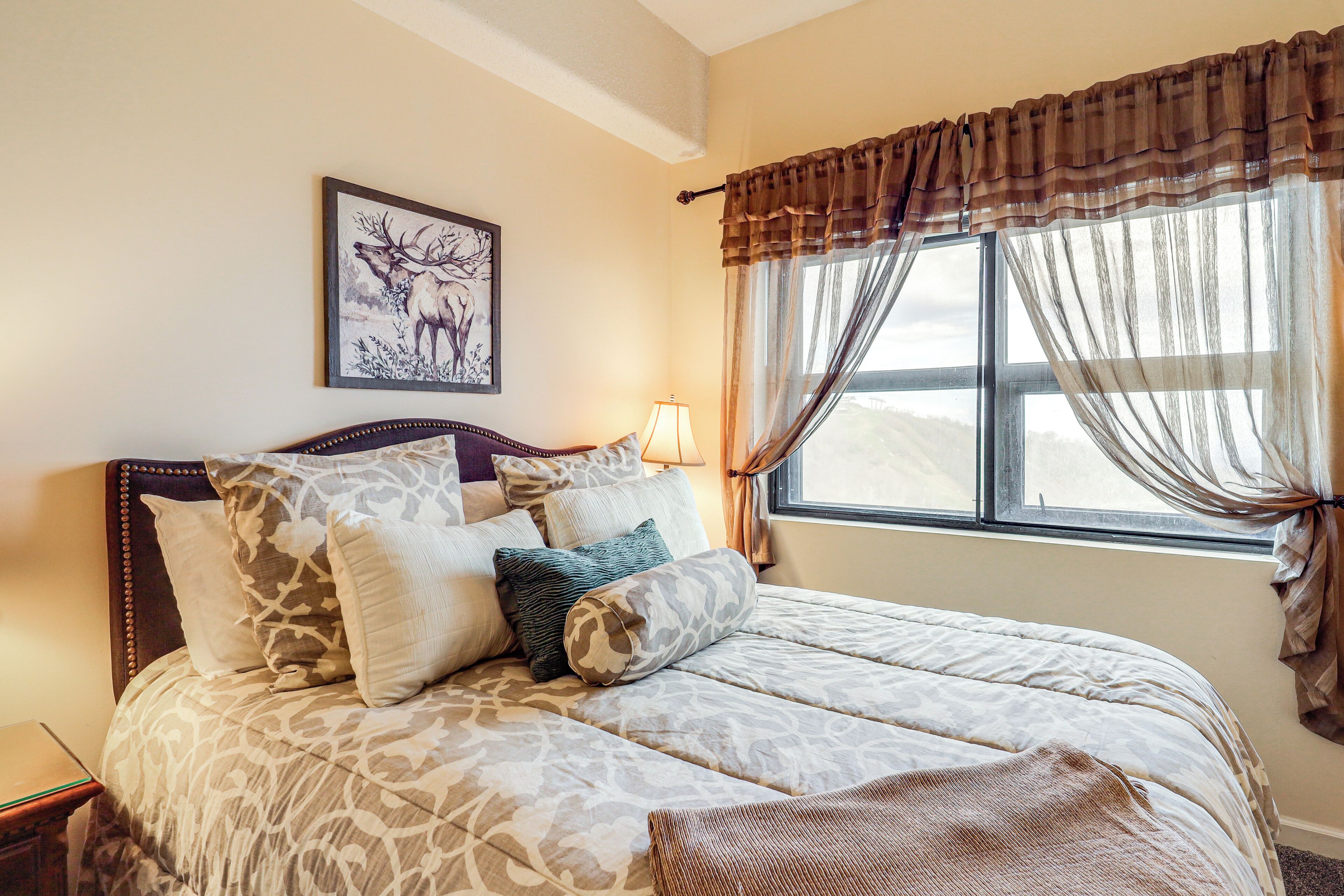 A bed with patterned bedding, a headboard, and a wall-mounted picture of an elk.
