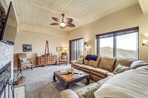 Un salón espacioso con un sofá grande, una mesa de centro y una chimenea. Amplias ventanas ofrecen vistas al exterior.