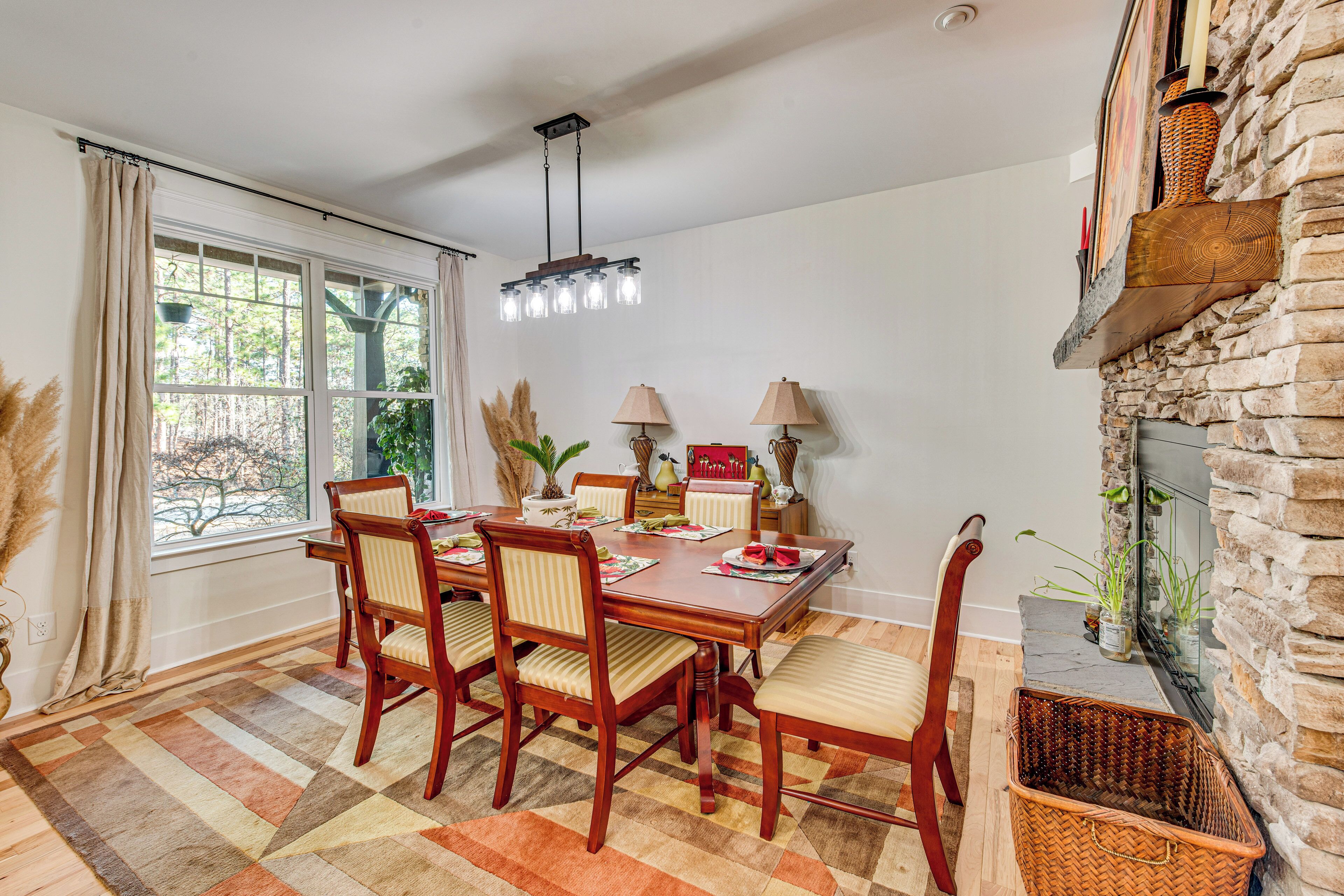 Une salle à manger avec une table en bois, six chaises, un lustre et une cheminée en pierre.