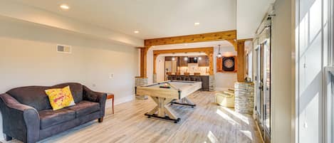 Un vaste espace de vie comprenant une table de billard, un canapé en cuir foncé et un mur décoratif en bois.