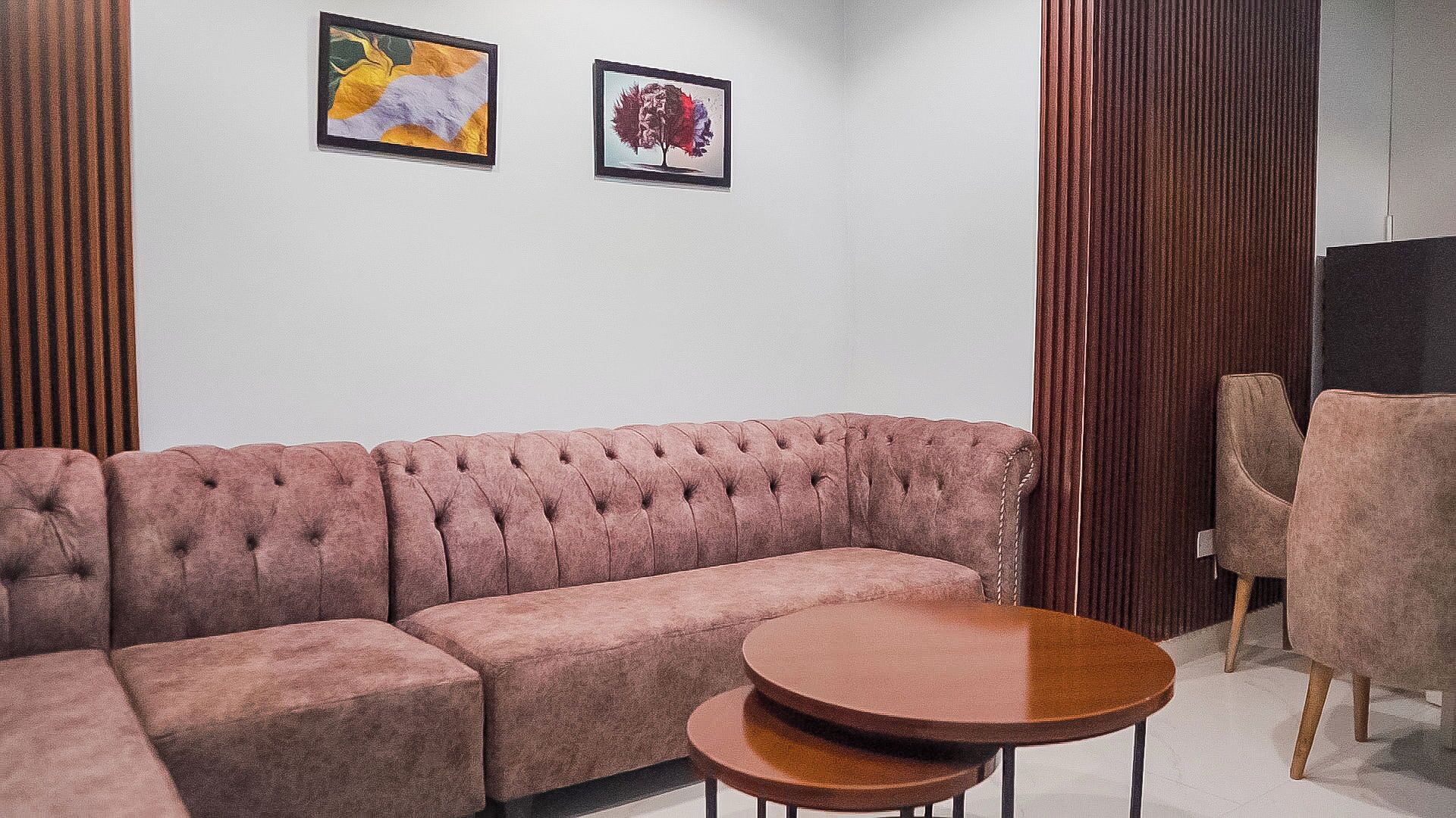 A living room with a pink sofa, two round wooden tables, and two framed artworks on the wall.