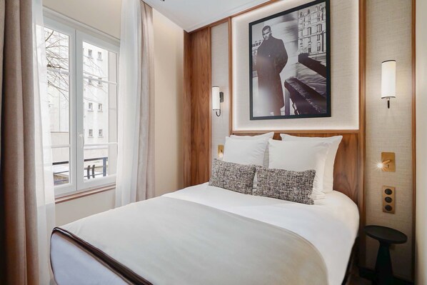 A hotel room with a large bed, a window with curtains, a framed picture on the wall, and a small table. - Merveil - Signature Suite - Champs Elysees - Dulud I (Neuilly-sur-Seine)