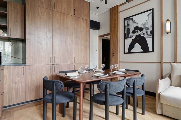 Un espace repas moderne avec une table en bois dressée pour quatre personnes, entourée de chaises aux couleurs sombres.