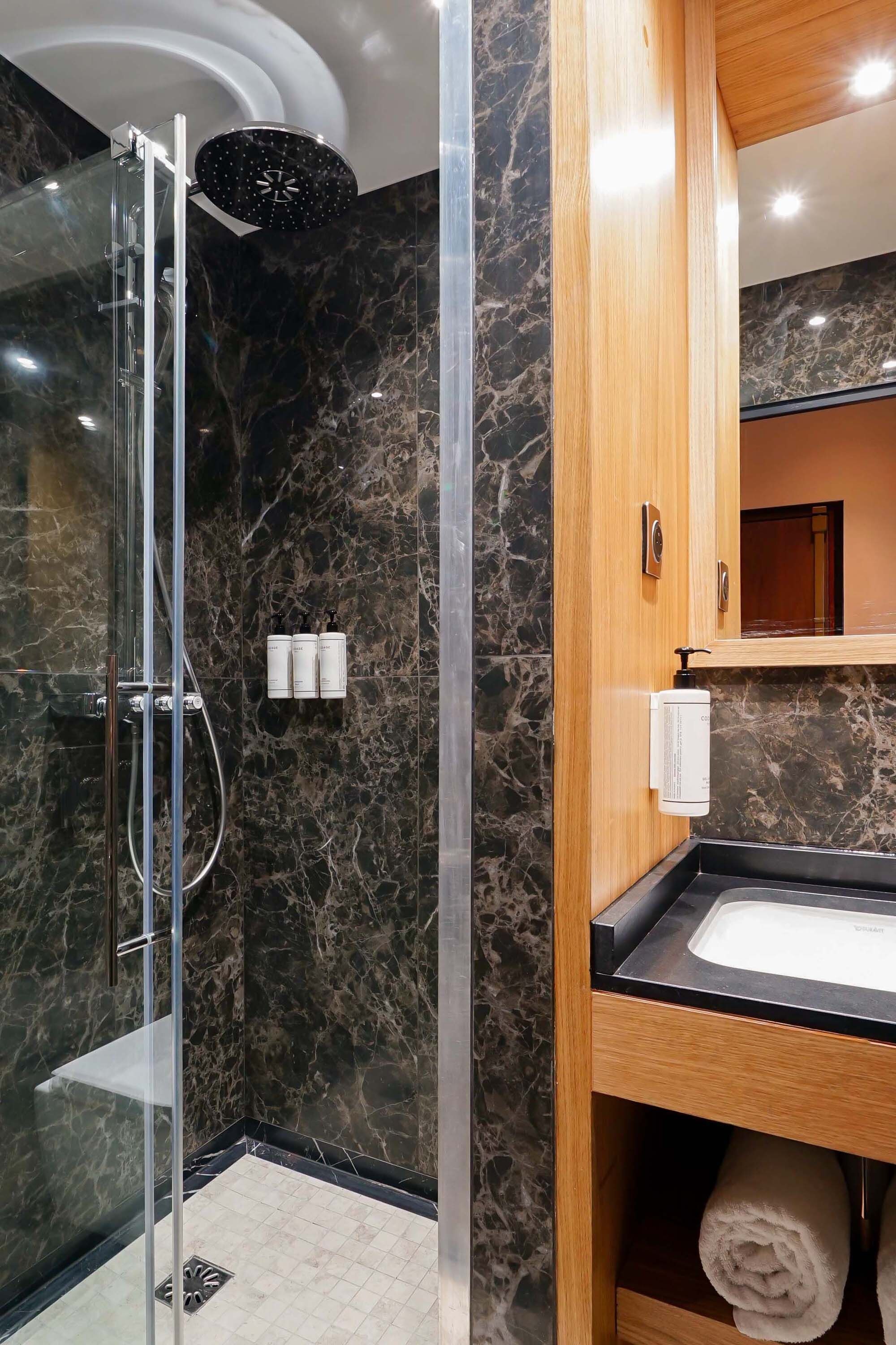 Une salle de bain moderne avec une douche à parois de verre, des murs en marbre, un meuble-lavabo en bois et un miroir au-dessus.