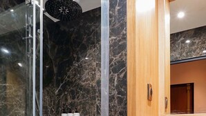 A modern bathroom with a glass-enclosed shower, marble walls, a wooden vanity with a sink, and a mirror above it. - Merveil - Signature Suite - Champs Elysees - Dulud I (Neuilly-sur-Seine)