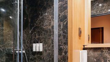 Une salle de bain moderne avec une douche à parois de verre, des murs en marbre, un meuble-lavabo en bois et un miroir au-dessus.