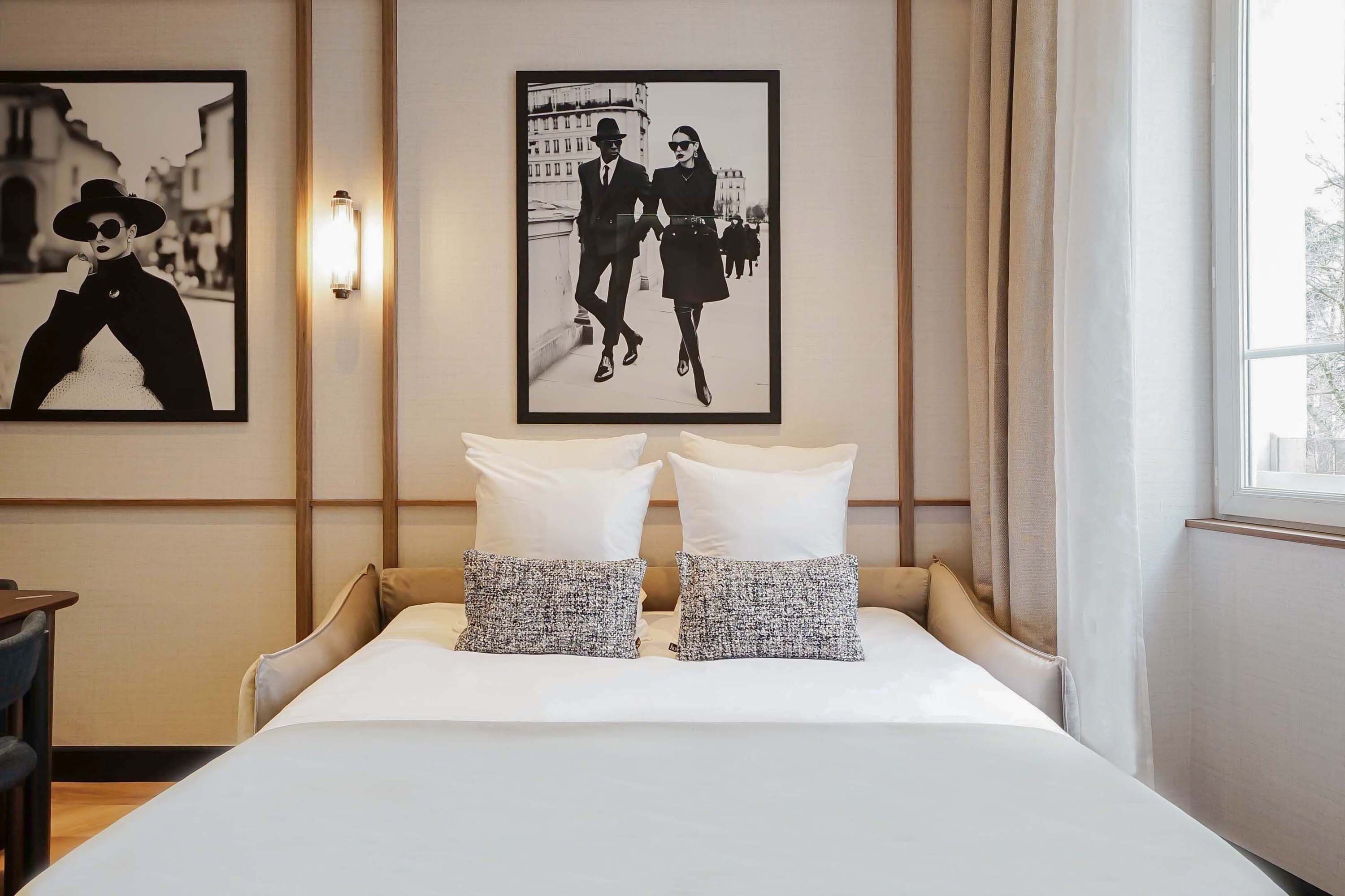 A hotel room with a bed, two pillows, a nightstand, a lamp, and two framed pictures on the wall.
