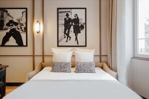 Une chambre d’hôtel avec un lit, deux oreillers, une table de chevet, une lampe et deux tableaux encadrés au mur.