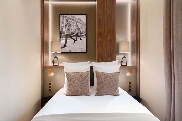 Una cama bien hecha con dos almohadas, un cuadro enmarcado encima y dos lámparas de noche.