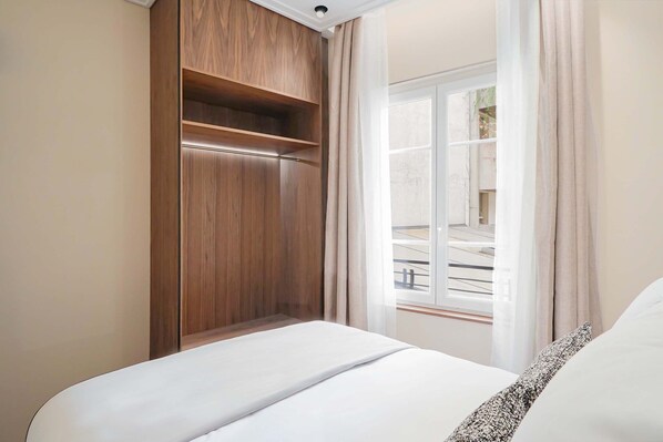A hotel room with a bed, a wooden wardrobe, and a window with curtains.