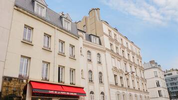 Un immeuble à plusieurs étages qui abrite au rez-de-chaussée un café appelé « Café de la Porte des Sablons ».