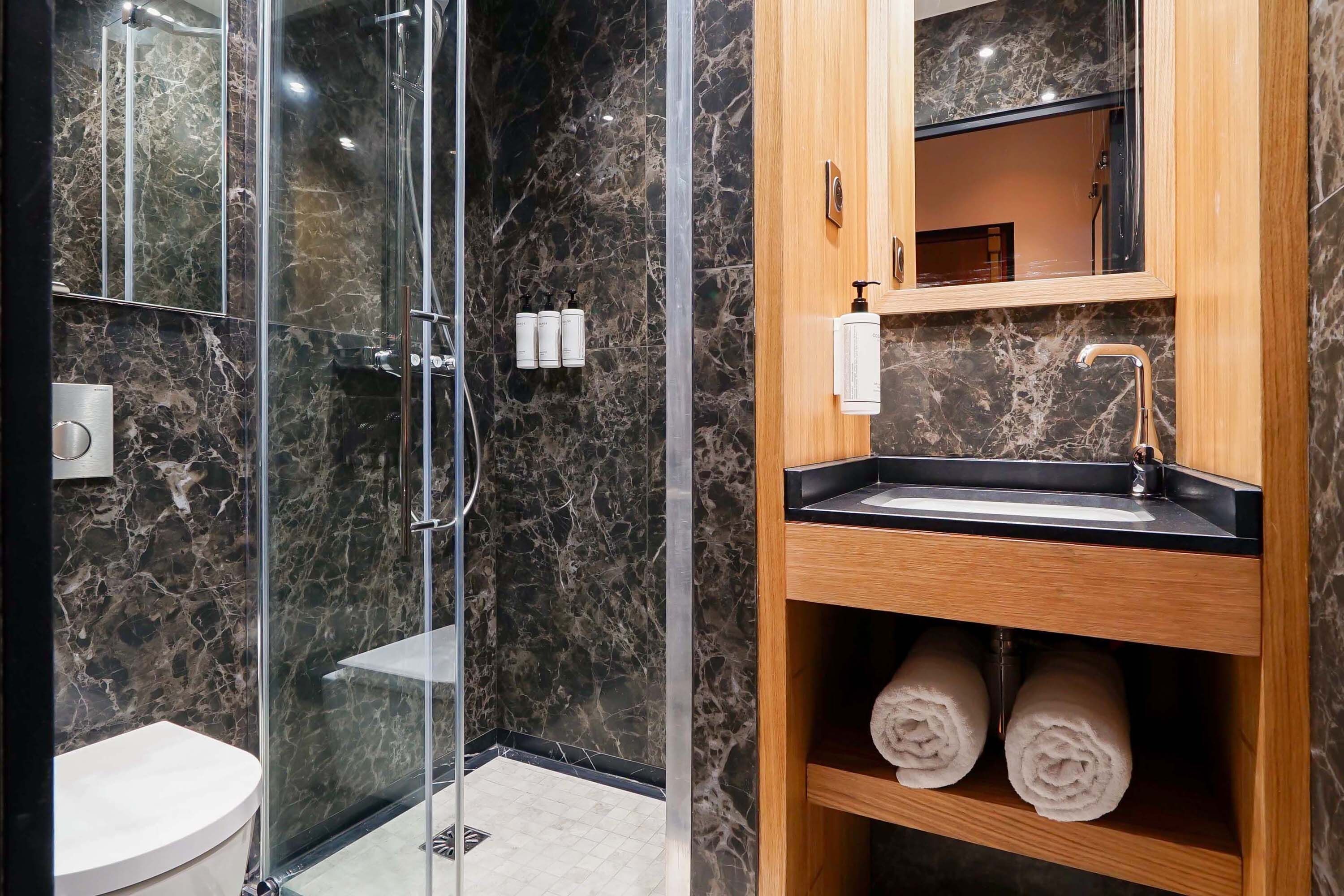 A modern bathroom with a glass-enclosed shower, a wooden vanity with a sink, and marble walls.