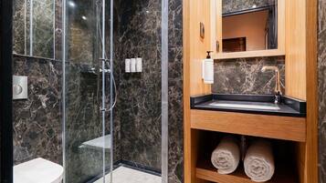 A modern bathroom with a glass-enclosed shower, a wooden vanity with a sink, and marble walls.