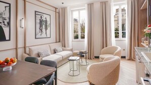A modern living room with a sofa, armchairs, a dining table, and a view of the city through large windows.