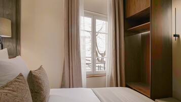 Une chambre d’hôtel avec un lit, une fenêtre avec des rideaux, une armoire en bois et une lampe.