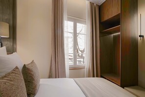 Une chambre d’hôtel avec un lit, une fenêtre avec des rideaux, une armoire en bois et une lampe.