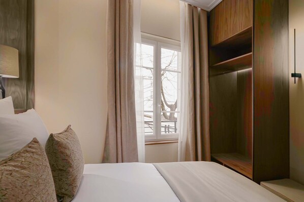 A hotel room with a bed, a window with curtains, a wooden wardrobe, and a lamp.