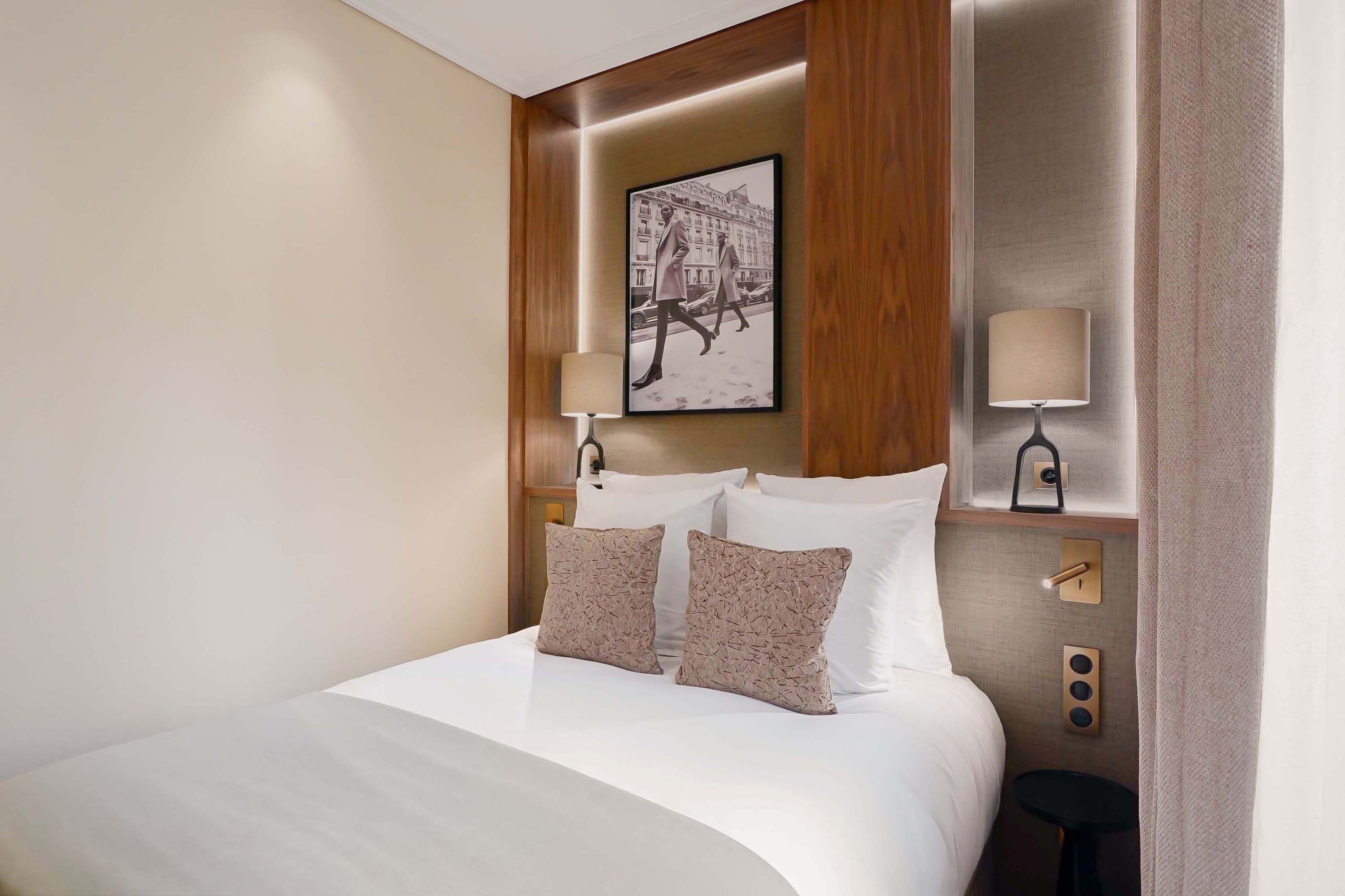 A neatly made bed with two pillows, a framed picture above it, and a small table beside the bed.