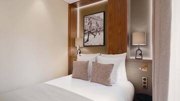 A neatly made bed with two pillows, a framed picture above it, and a small table beside the bed.