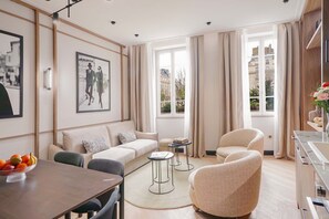 Una sala moderna con un sofá, dos sillones, una mesa de comedor con fruta y una zona de cocina con un fregadero y armarios.
