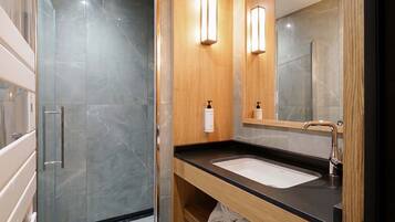 A modern bathroom with a glass shower enclosure, a wooden vanity with a black countertop, and a large mirror.