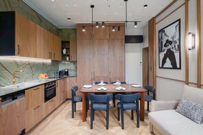A modern kitchen with wooden cabinets, a marble countertop, and a dining area with a table set for six. - Merveil - Signature Suite - Champs Elysees - Dulud I (Neuilly-sur-Seine)