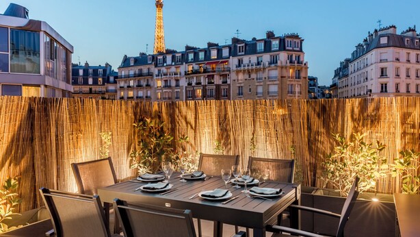 An outdoor dining area with a view of the Eiffel Tower, bamboo wall, and European-style buildings.