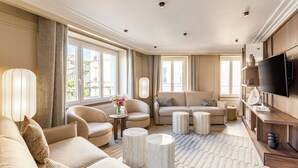 A spacious living room with a sofa set, two armchairs, a coffee table, and a TV.