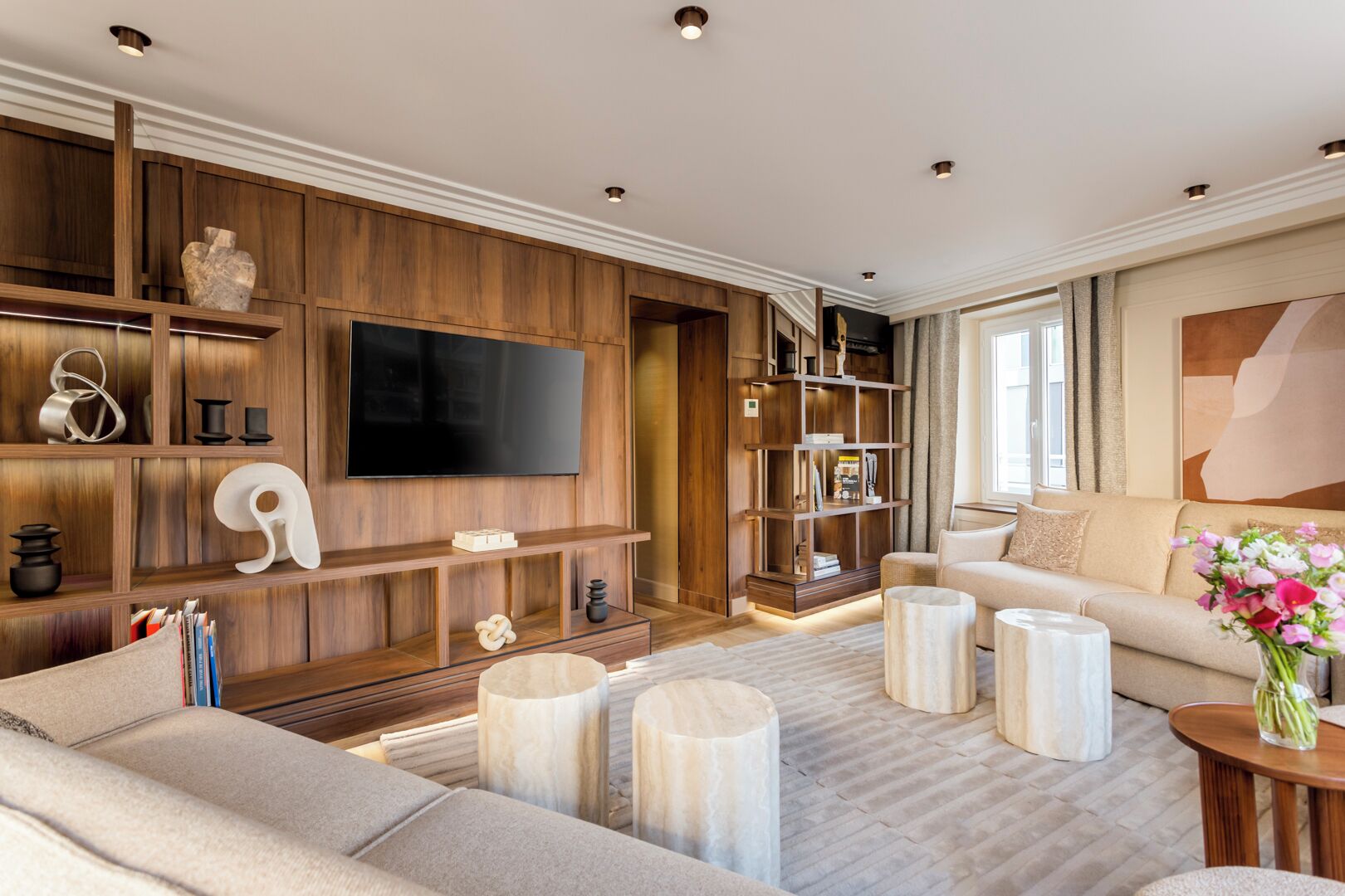 Een moderne woonkamer met een grote flatscreen-tv, houten lambrisering, een beige bank en een salontafel.
