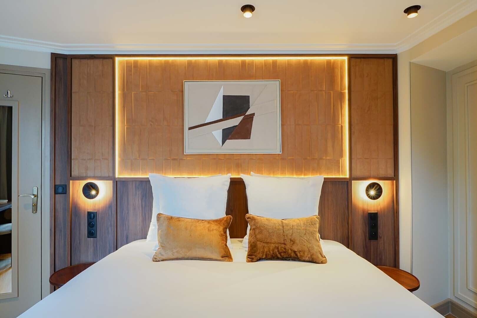 A modern bedroom with a large bed, two side tables, a wall-mounted artwork, and recessed lighting.