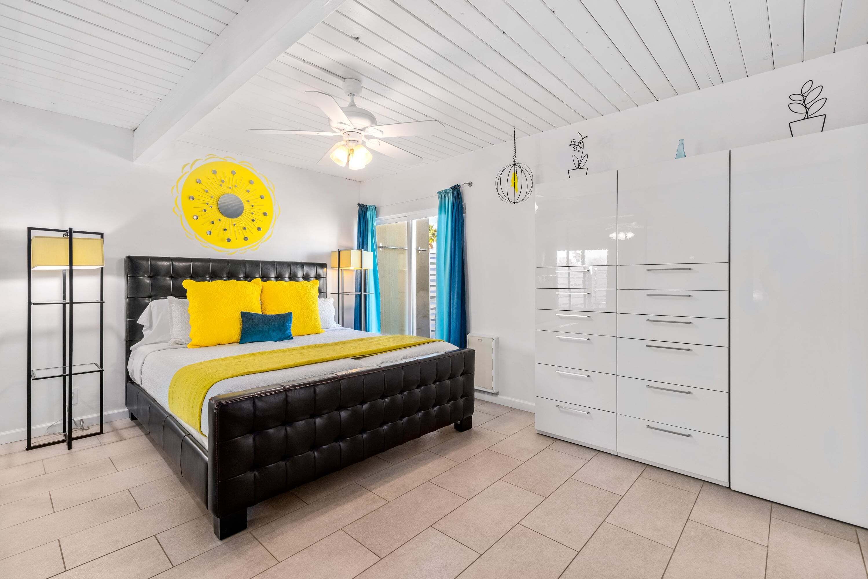 Een slaapkamer met een zwart bed, een witte kledingkast en een plafondventilator.